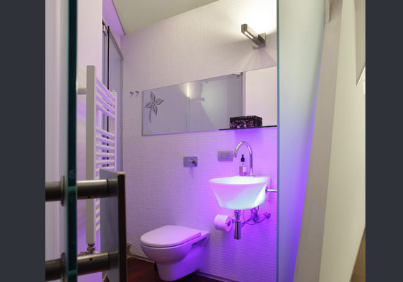 Il toilette, volume in vetro sabbiato, sporge dietro le pareti e, attraverso un lavabo illuminato